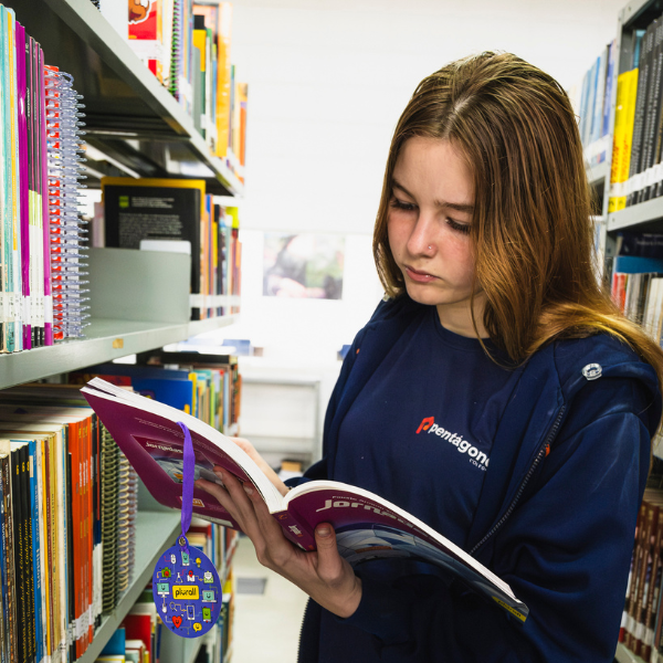 Aluna do Colégio Pentágono lendo livro entre as estantes da biblioteca