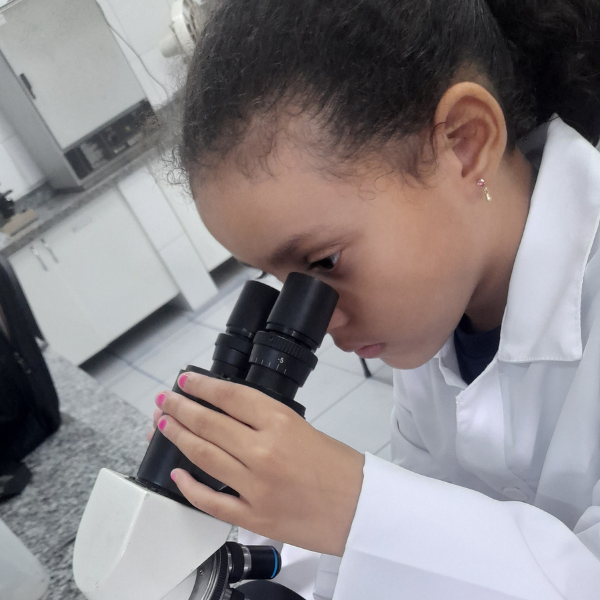 Aluna de jaleco observando lâmina no microscópio do laboratório