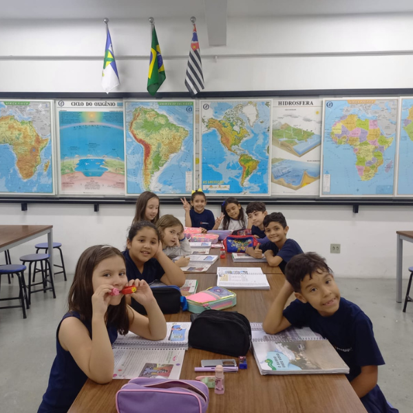 Alunos em sala de aula com mapas-múndi e bandeiras ao fundo