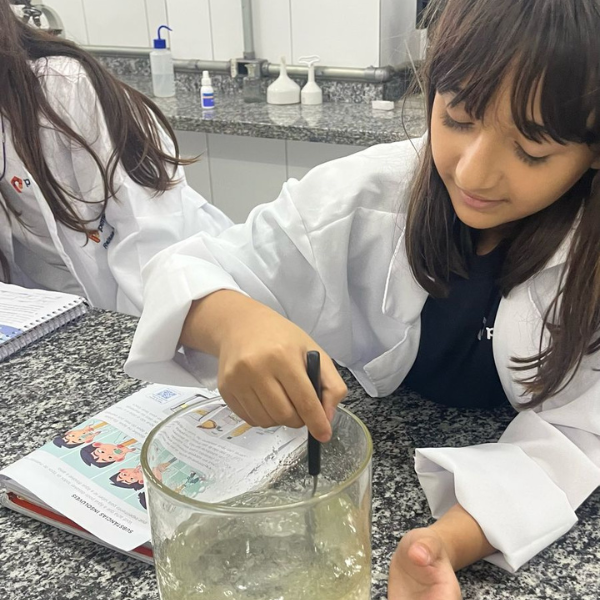Alunas de jaleco realizando experimento com béquer no laboratório de ciências