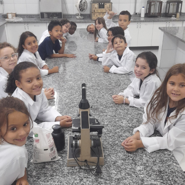 Turma de jaleco reunida ao redor de microscópio no laboratório de ciências