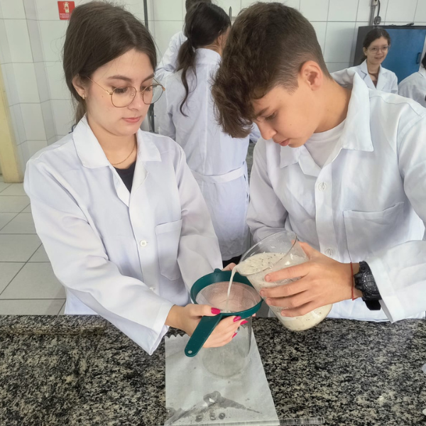 Estudantes de jaleco pesando amostra em aula prática de Química