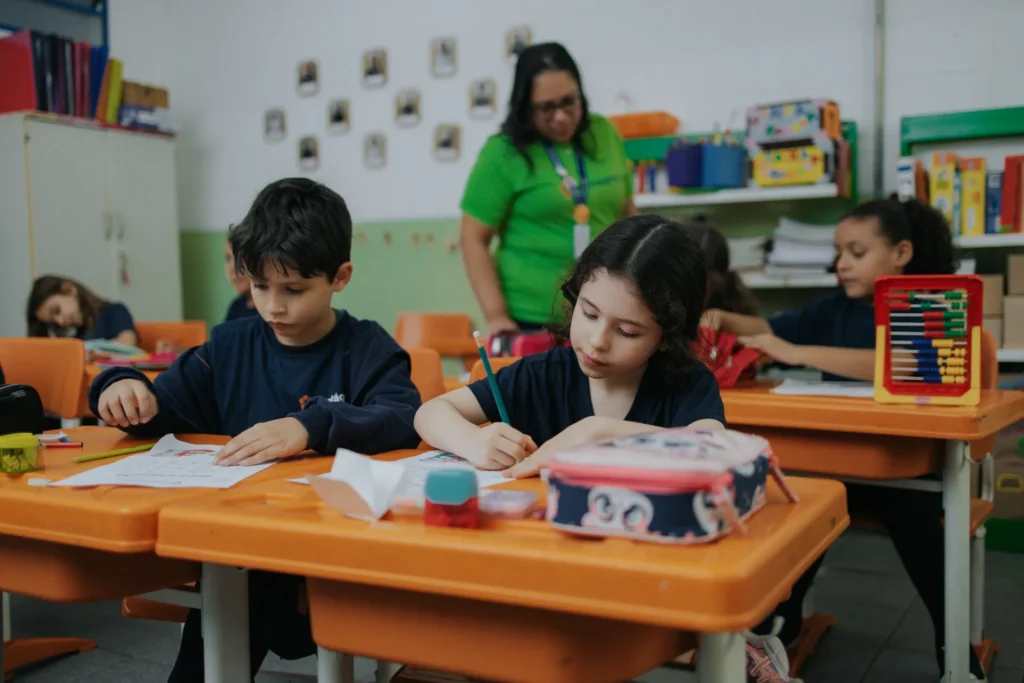 Alunos dos Anos Iniciais em atividade escrita acompanhados pela professora